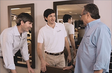 Three people standing and talking in front of two large mirrors.