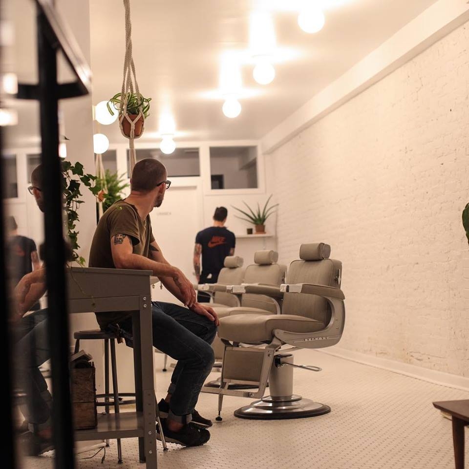 Interior view of Mildred New York barbershop showing white ceiling, walls, and floor, and gray salon chairs.